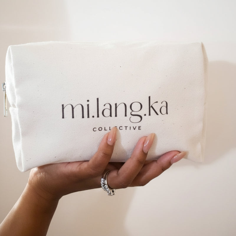 Hand holding a beige pouch with 'mi.lang.ka collective' branding against a neutral background